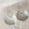 Close-up of sterling silver pear-shaped hammered dangle earrings with French hook ear wires on a marble surface.

